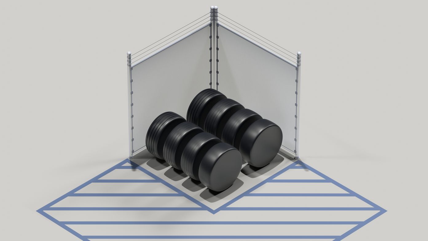 Tires surrounded by a tall fence with a privacy screen and topped with barbed wire. Striped pavement surrounds the fence.
